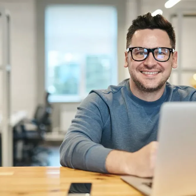 man in long sleeve shirt smiling with glasses looking at you